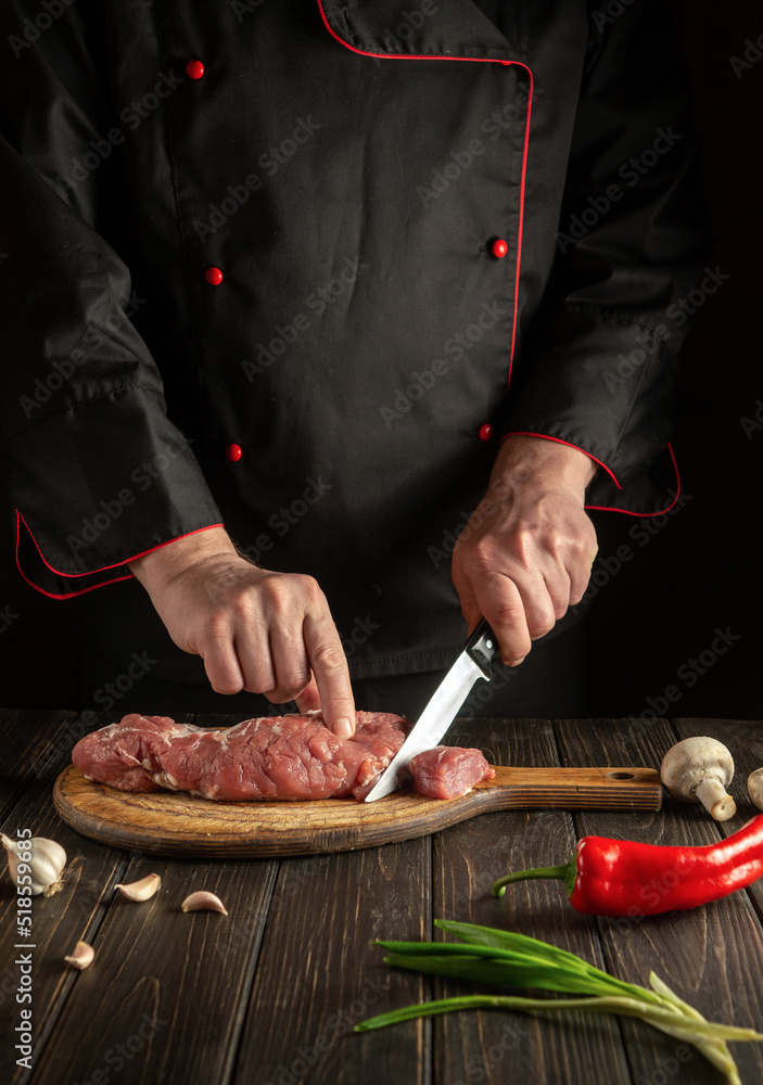 Chef cuts raw beef meat on a cutting board before baking. Free space for hotel menu or recipe