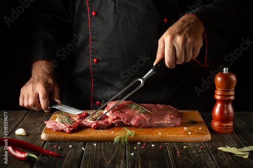 Cooking raw beef meat by hands of a chef on a kitchen cutting board. Idea for a hotel menu on a dark background
