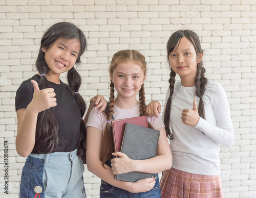 Three female students at an international school stand and thumb up