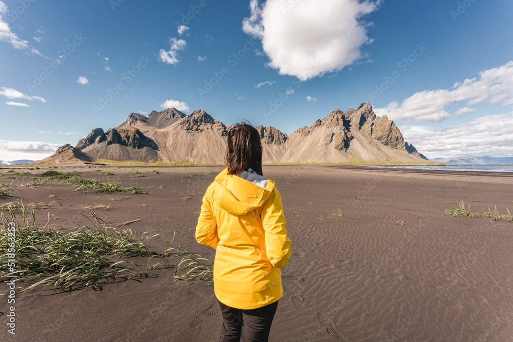 Young asian woman in yellow jacket standing on the beach with Vestrahorn mountain in viking village on Stokknes at Iceland Young asian woman in yellow jacket standing on the beach with Vestrahorn mountain in viking village on Stokknes at Iceland