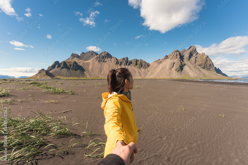 Young asian woman in yellow jacket holding hands with boyfriend on the beach with Vestrahorn mountain in viking village on Stokknes at Iceland Young asian woman in yellow jacket holding hands with boyfriend on the beach with Vestrahorn mountain in viking village on Stokknes at Iceland