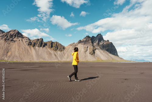 Young asian woman in yellow jacket standing on the beach with Vestrahorn mountain in viking village on Stokknes at Iceland photo