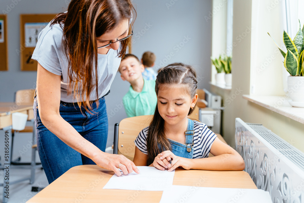 Teacher helping cute little girl with writing lesson at classroom. Teacher helping cute little girl with writing lesson at classroom.