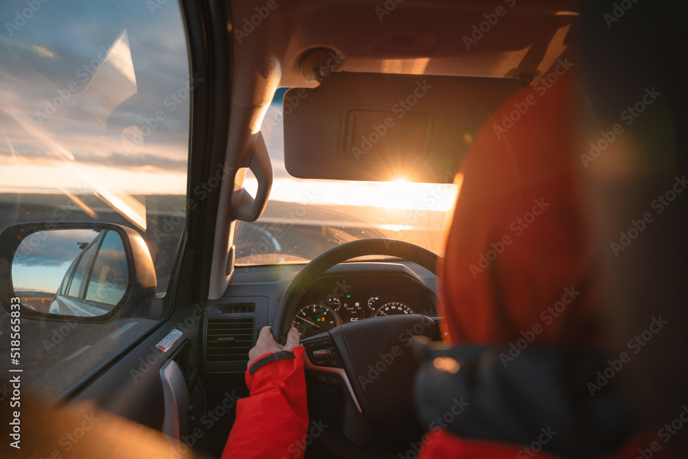 Fototapeta premium Man driving a car through wilderness on asphalt road in the sunset