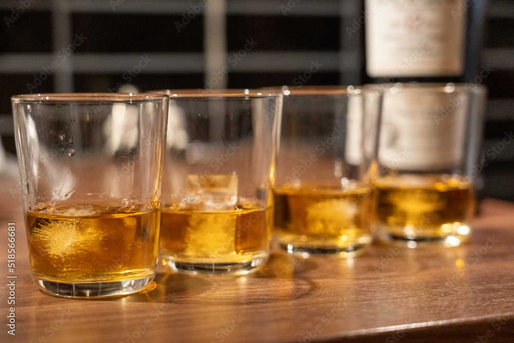 Whiskey glasses on a table, half filled with whiskey bottle blurred in the background Whiskey glasses on a table, half filled with whiskey bottle blurred in the background