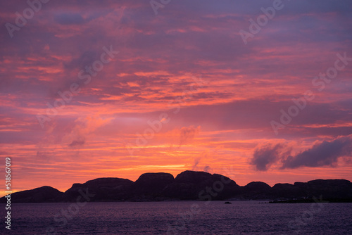 Beautiful orange  red and purple Norwegian sunset with colored clouds and an ocean with mountain in the background 