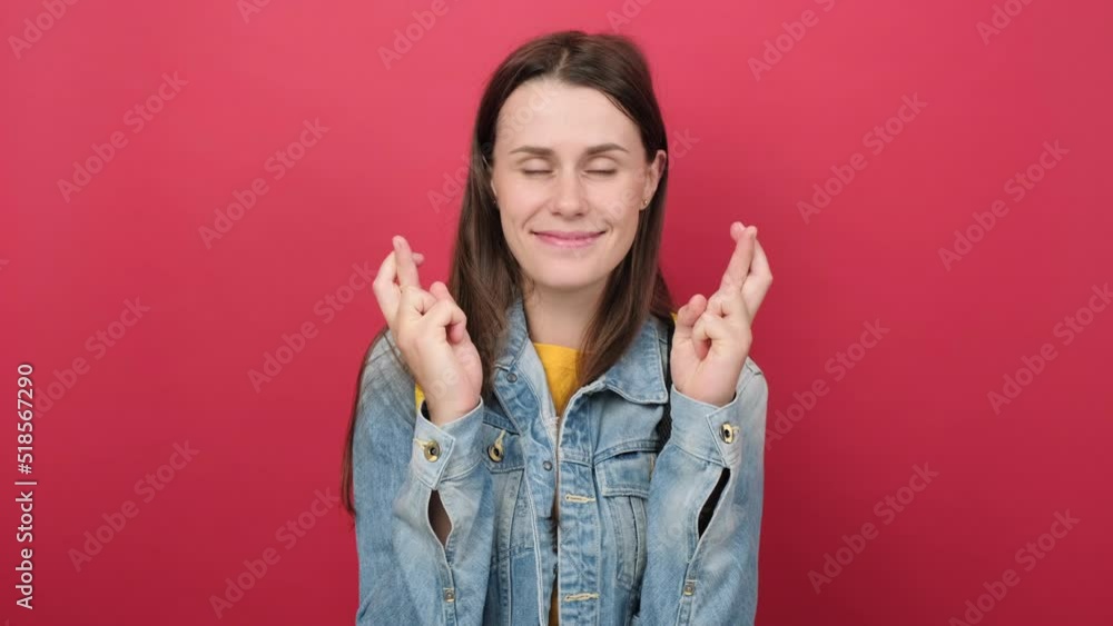 Cute young girl teen student in denim jacket and yellow backpack keep finger cross making with eyes closed, posing isolated on red background wall. Education in high school university college concept Cute young girl teen student in denim jacket and yellow backpack keep finger cross making with eyes closed, posing isolated on red background wall. Education in high school university college concept