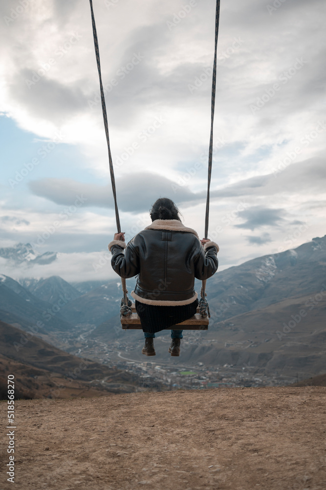 Young girl swinging on a homemade swing Against the backdrop of cloudy sky and mountain hills Young girl swinging on a homemade swing Against the backdrop of cloudy sky and mountain hills