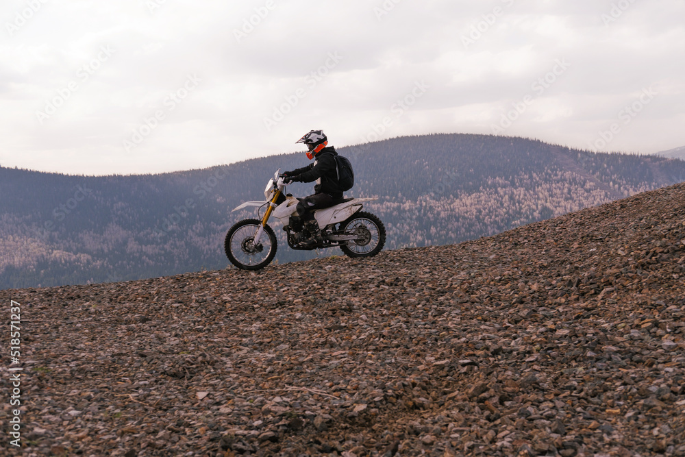 Motorcyclist riding off-road motorcycle on gravel rocky slope in mountains hills