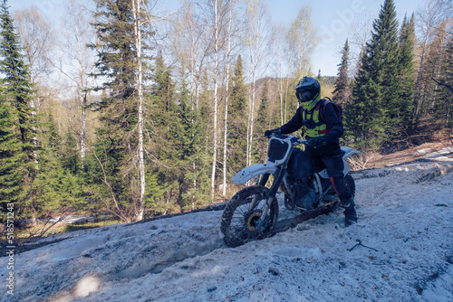 Rider riding dirt motorcycle on snowy off-road on summer day in mountains