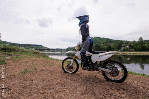 Beautiful slender girl wearing  helmet and moto protection turtle on  motorcycle in a rack on the lake photo