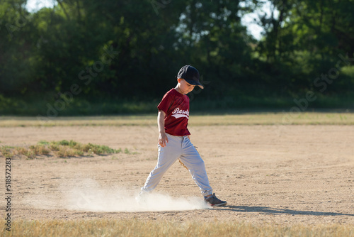 A little boy playing baseball kicking up dirt wearing a baseball glove