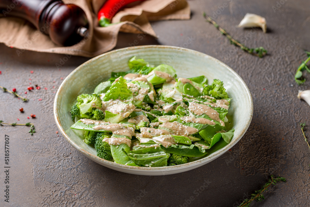 Green vegetable salad with broccoli and greenery with sauce on brown table Green vegetable salad with broccoli and greenery with sauce on brown table