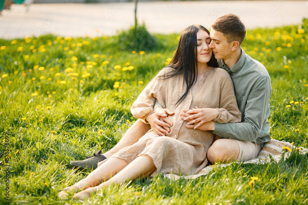 Pregnant woman and her husband sitting in a park on a grass and hugging Pregnant woman and her husband sitting in a park on a grass and hugging