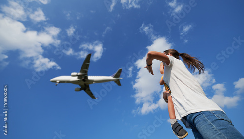 Bottom view of woman with toddler waving hand to landing commercial airplane in the sky. Lifestyle and travel concept.
