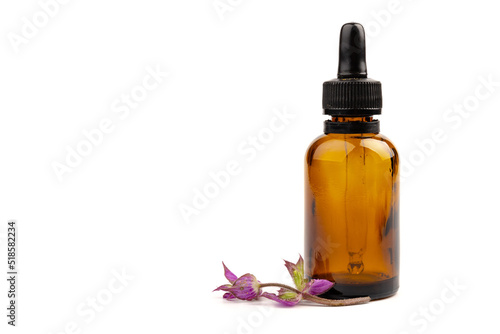 A bottle of essential oil with fresh blooming clary sage twigs on white background.