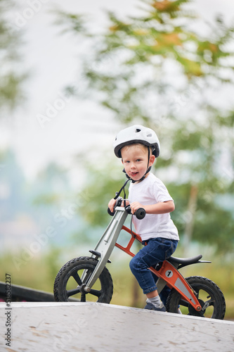 Portrait of child riding balance bike. Male toddler kid in helmet learning to ride on run bicycle at skate park. © anatoliy_gleb