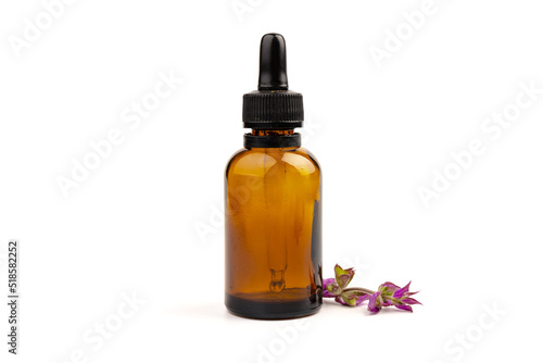 A bottle of essential oil with fresh blooming clary sage twigs on white background.
