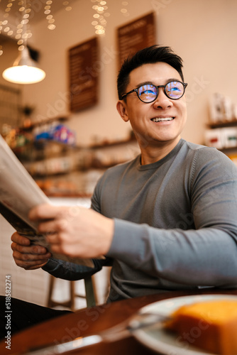 Adult asian man reading newspaper while having breakfast in cafe