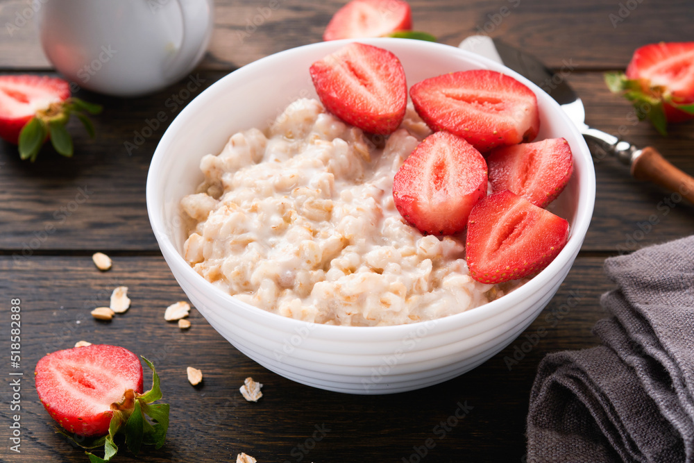 Oatmeal. Bowl of oatmeal porridge with strawberry, almond and milk on old wooden dark table background. Top view in flat lay style. Natural ingredients. Hot and healthy breakfast and diet food. Oatmeal. Bowl of oatmeal porridge with strawberry, almond and milk on old wooden dark table background. Top view in flat lay style. Natural ingredients. Hot and healthy breakfast and diet food.