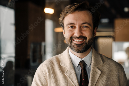 Fototapeta Portrait of happy bearded businessman in jacket looking in camera