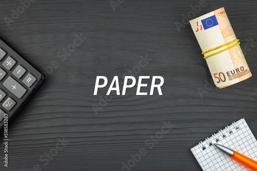 PAPER - word (text) and euro money on a wooden background, calculator, pen and notepad. Business concept (copy space).