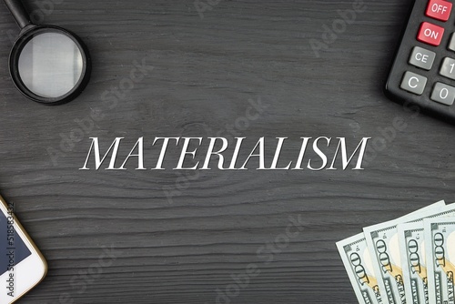 Foto MATERIALISM - word (text) and money dollars on the table, phone magnifying glass (loupe) and calculator