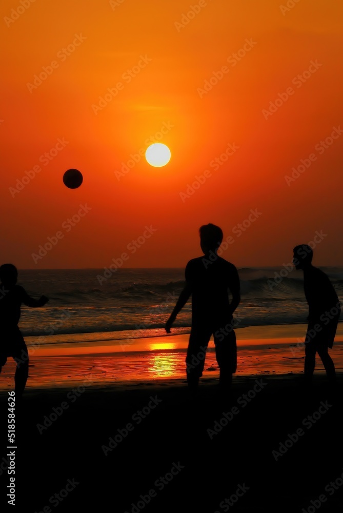 silhouettes of people playing footbal on the beach when sunset