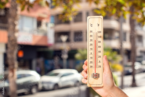 Hot weather. Thermometer in front of an urban scene during heatwave.