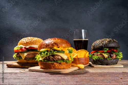 Tasty homemade burger. Set of tasty cheeseburger, beef and ham burger with fresh vegetables, mouth-watering delicious sauce, on dark wooden background copy space