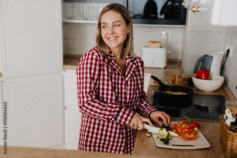 Young happy woman cutting vegetables while cooking at home