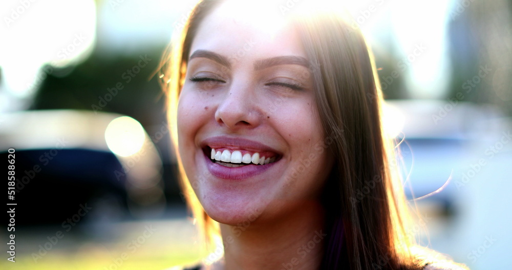 Young woman portrait smiling with lens-flare outside. Millennial girl real life smile and laugh outdoors sunflare
