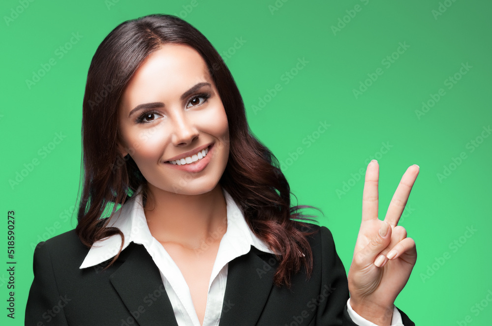 Businesswoman in black suit, showing two fingers or victiory gesture, isolated on green background. Portrait of happy smiling cheerful young business woman. Businesswoman in black suit, showing two fingers or victiory gesture, isolated on green background. Portrait of happy smiling cheerful young business woman.