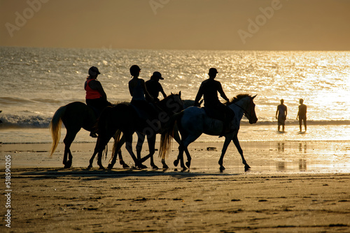 silhouettes of people enjoying summer holidays horse riding on the beach