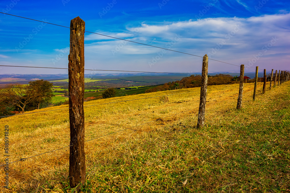 Φωτογραφία Wooden and wire fence on top of a hill with the landscape of pastures and plantations in the background in a sunny day and blue sky