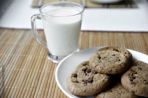 A glass glass with milk on a wooden mat with oatmeal cookies. Afternoon lunch with cookies. Sweet cookies with milk.