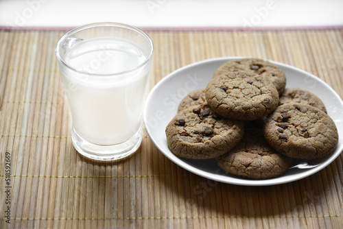 A glass glass with milk on a wooden mat with oatmeal cookies. Afternoon lunch with cookies. Sweet cookies with milk.