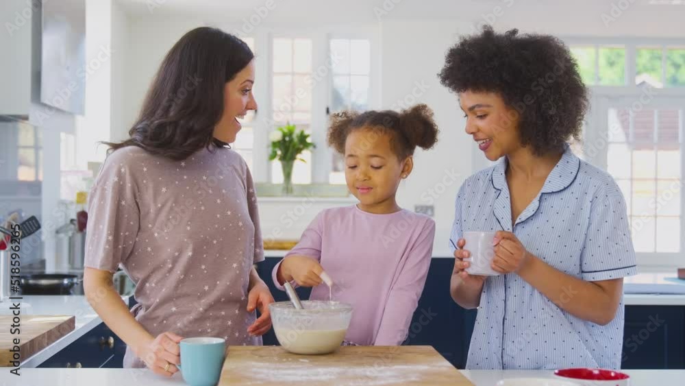 Daughter in family with two Mums putting pancake mixture on woman's nose as they make breakfast together - shot in slow motion