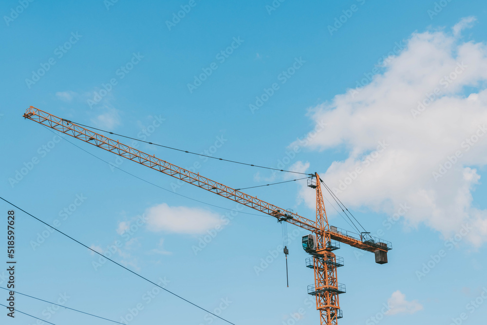 Yellow construction tower crane against blue sky.House under construction. Industrial skyline.