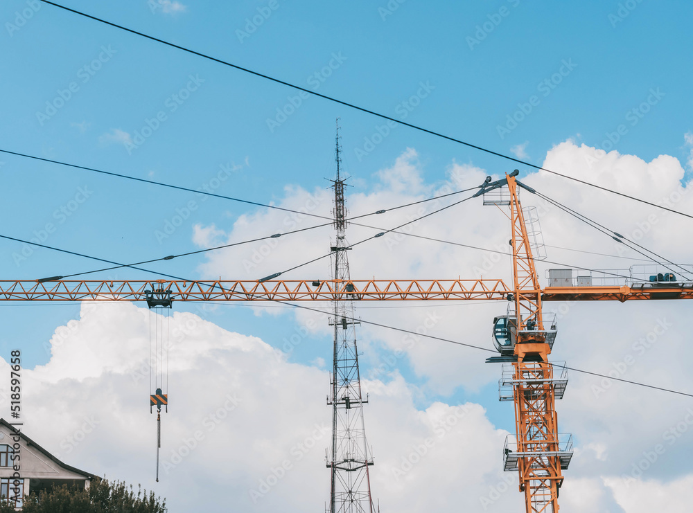 Yellow construction tower crane against blue sky.House under construction. Industrial skyline. Yellow construction tower crane against blue sky.House under construction. Industrial skyline.
