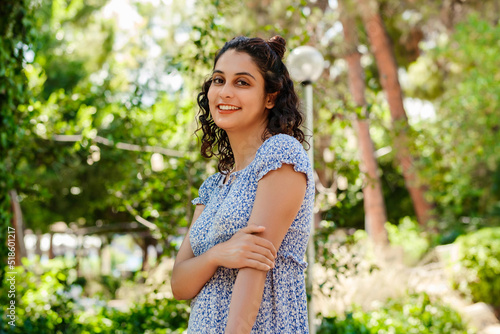 Portrait of cute brunette woman wearing a blue floral summer dress standing on city park, outdoors looking at camera while posing. Natural beauty concept. Beautiful girl. Pretty young woman.