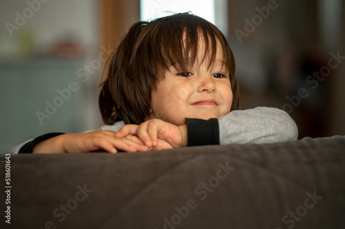 Portrait of a three-year-old boy with long dark hair, at home. Cute smiling kid © Anastasia Amraeva