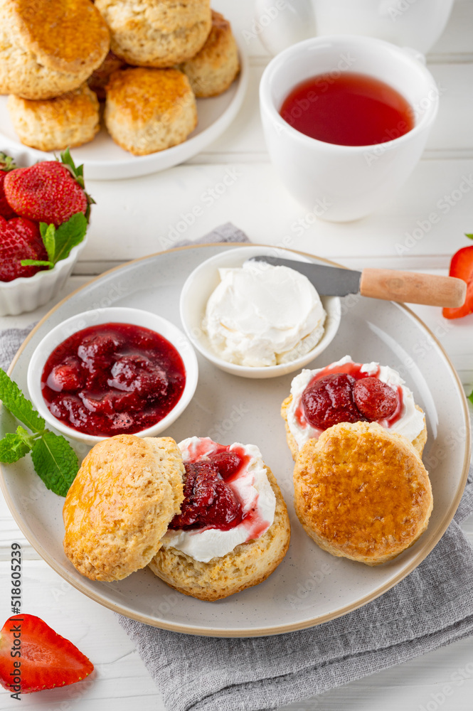 Homemade British Scones with cream cheese, strawberry jam and a cup of tea on a white wooden background. Homemade British Scones with cream cheese, strawberry jam and a cup of tea on a white wooden background.