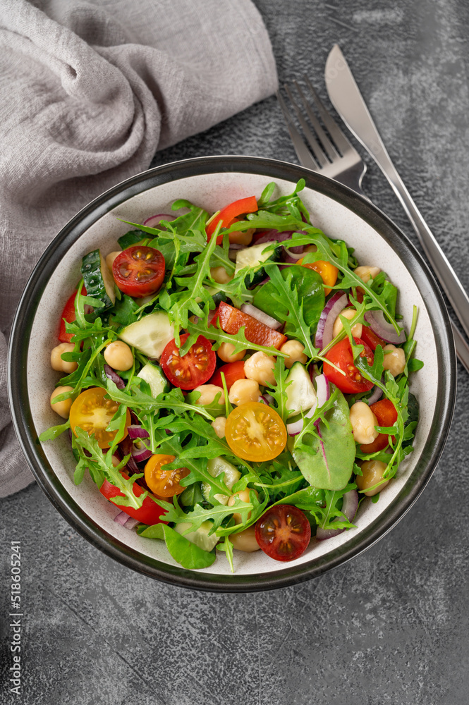 Salad with chickpeas, green leaves and fresh vegetables in a bowl on a gray concrete background. Healthy food. Top view, copy space. Salad with chickpeas, green leaves and fresh vegetables in a bowl on a gray concrete background. Healthy food. Top view, copy space.