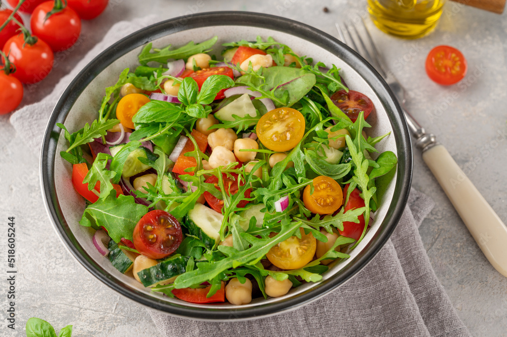 Salad with chickpeas, green leaves and fresh vegetables in a bowl on a gray concrete background. Healthy food. Top view, copy space.