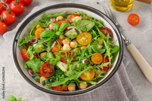 Salad with chickpeas, green leaves and fresh vegetables in a bowl on a gray concrete background. Healthy food. Top view, copy space.