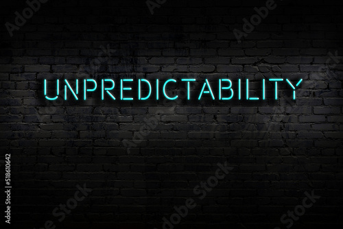 Neon sign. Word unpredictability against brick wall. Night view