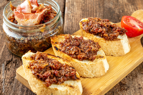 Homemade bacon jam on croutons and next to a jar of jam on an old wooden table.