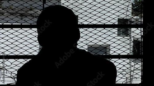Silhouette of an Inmate Looking Through Window Bars inside a Cell of An Old Prison in Buenos Aires Province, Argentina.