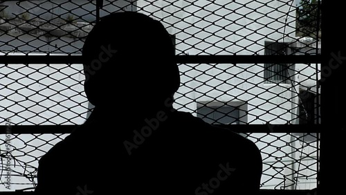 Silhouette of an Inmate Looking Through Window Bars inside a Cell of An Old Prison in Buenos Aires Province, Argentina. photo